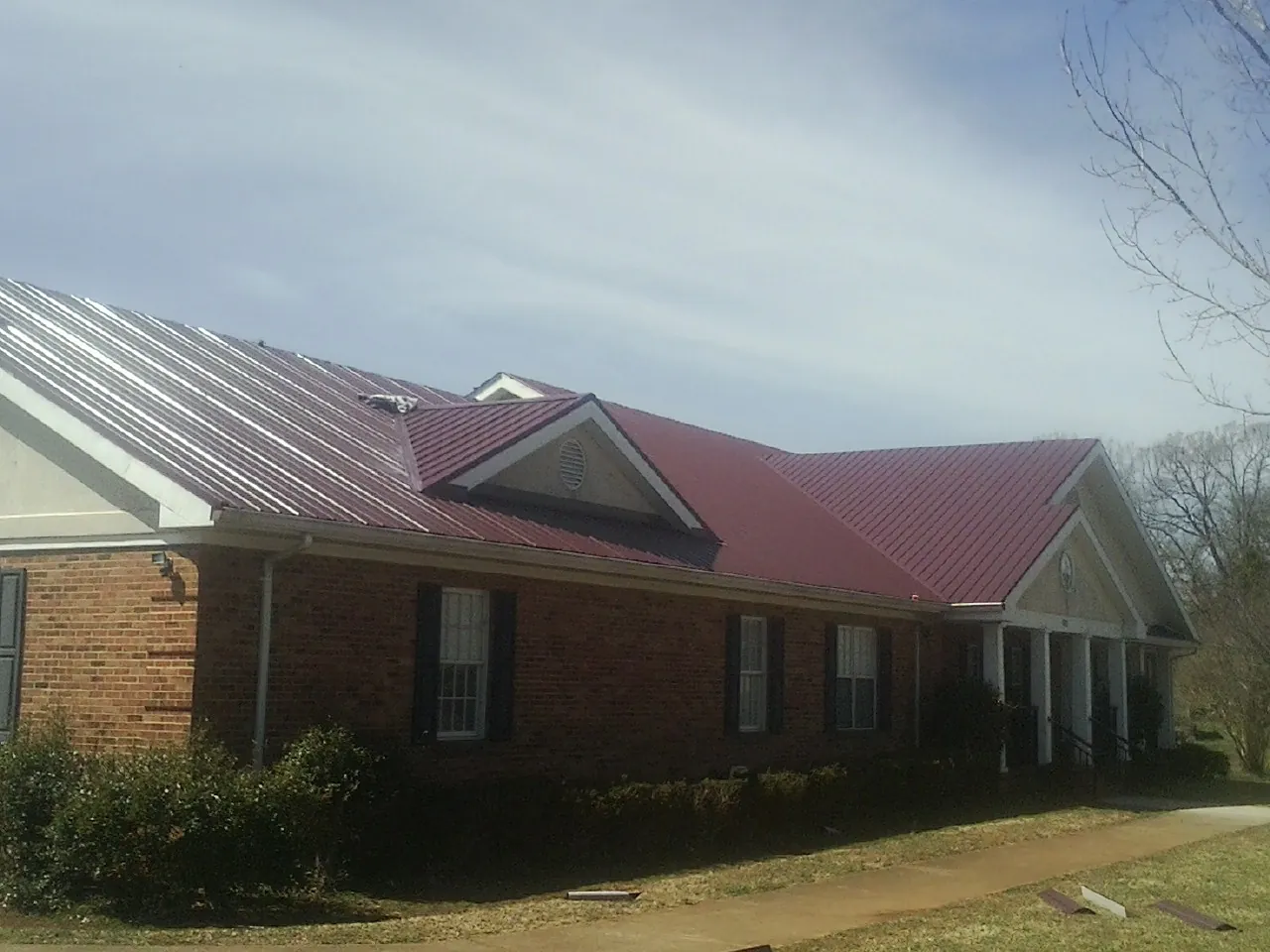 Red metal roof with gabled entries on a long brick building, from a Hail Damage Roof Repair job in Sandy Spring