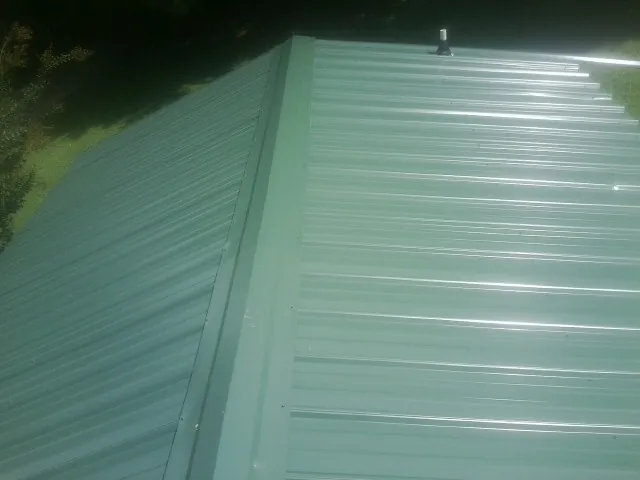 New green metal panels meeting at the ridge of a roof — Flat Roof Repair work by our crew in Sandy Spring