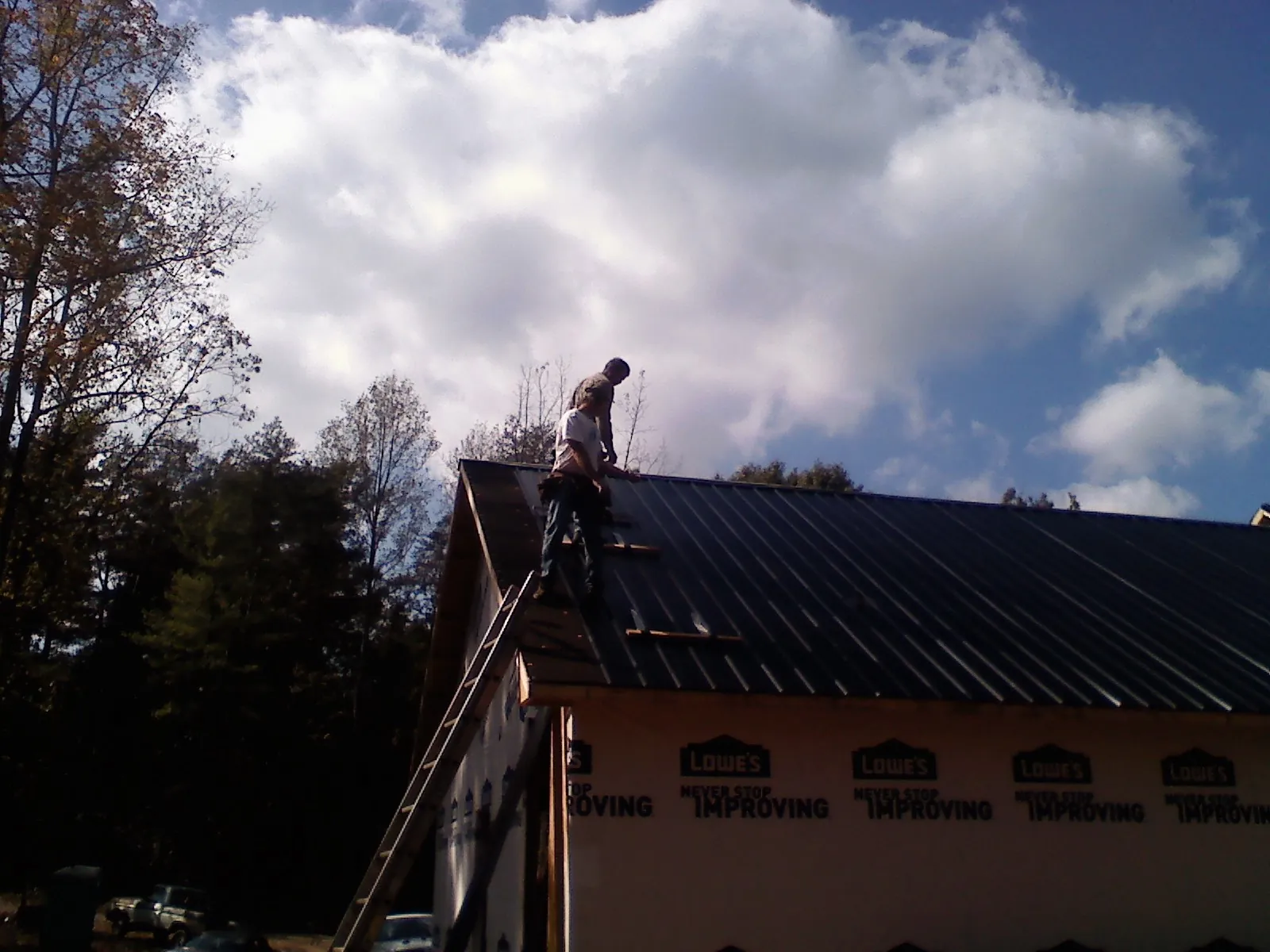 Roofer fastening dark metal panels high against a cloudy sky, from a Roof Inspection job in Sandy Spring