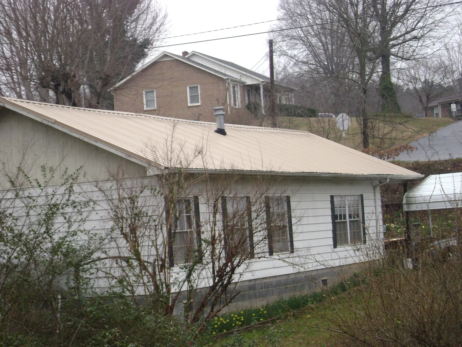 Tan metal roof on a white sided house set into a hillside — Commercial Roofing by Roofing Brothers in Sandy Spring